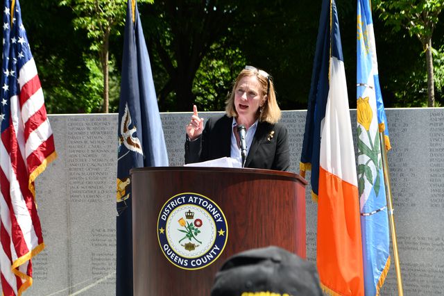 Photograph of Queens DA Melinda Katz speaking at a lectern, on a dais outside.